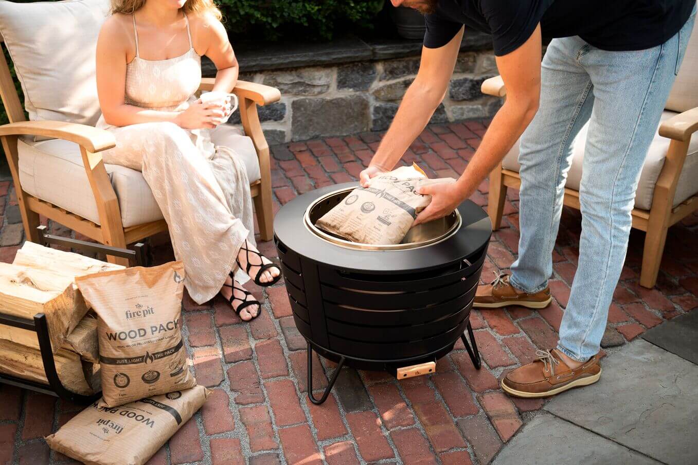 Man placing wood packs in the smokeless fire pit while woman enjoys a cup of coffee