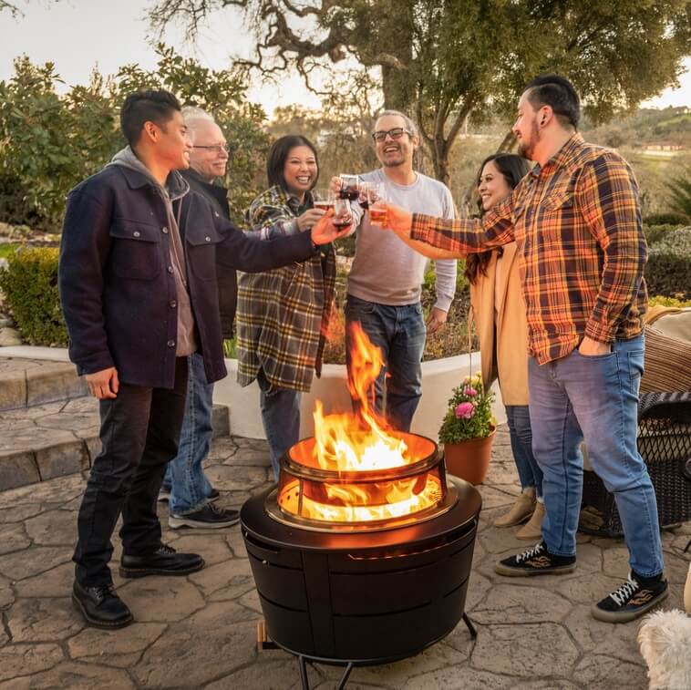 A group of friends cheersing and hanging out around the Reunion Smokeless Fire pit