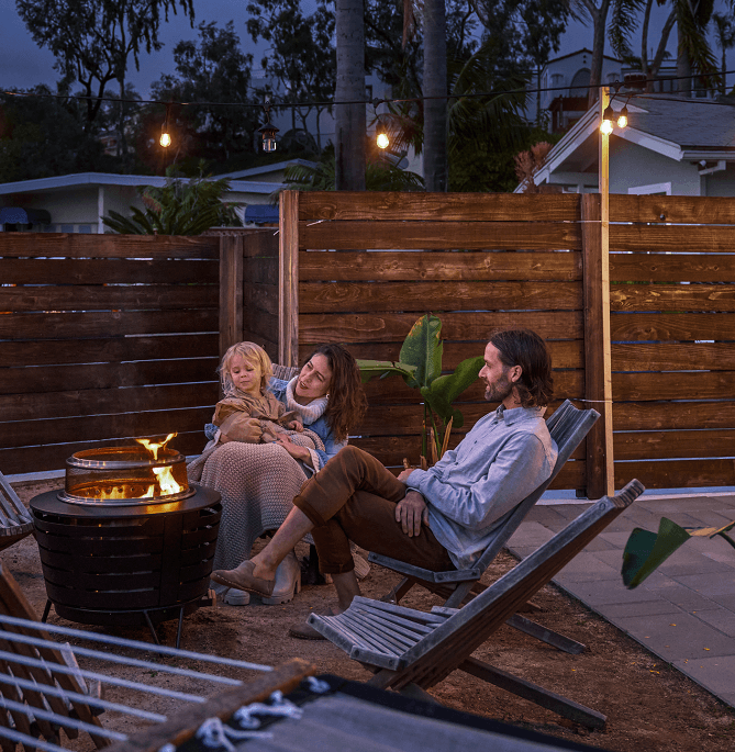 Family hanging out underneath mosquito repellent string lights around a smokeless fire pit